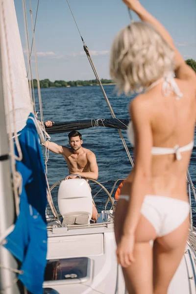 Selective focus of woman in bikini and her boyfriend standing behind on yacht — Stock Photo