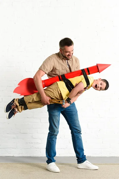 Père tenant fils avec fusée jouet sur le dos à la maison — Photo de stock