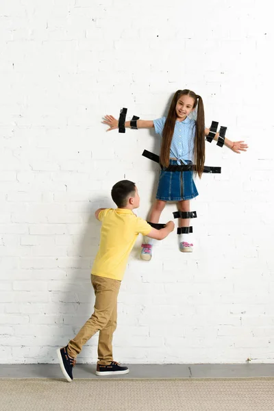 Brother gluing sister to wall with black tape at home — Stock Photo