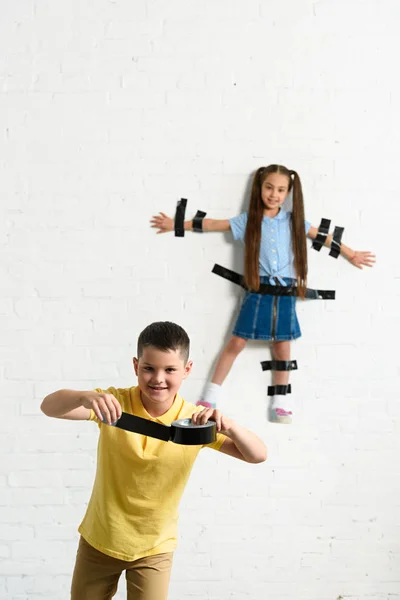 Disobedient brother glued sister to wall with black tape at home — Stock Photo