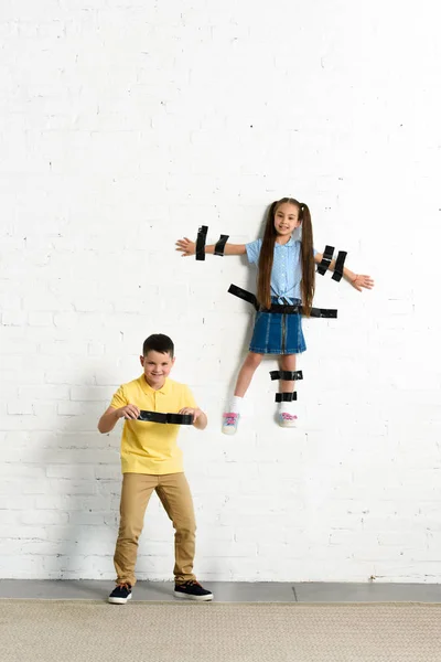 Brother glued sister to wall with black tape at home — Stock Photo