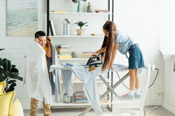 Fratrie désobéissante repassage vêtements à la maison — Photo de stock