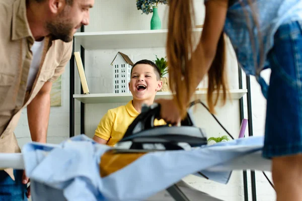 Chico riendo mientras su hermana ardiendo camisa con hierro en casa - foto de stock