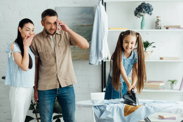 Hija sosteniendo hierro sobre camisa quemada en casa, concepto de paternidad - foto de stock