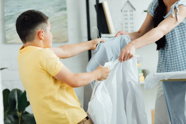 Cropped image of mother and son holding rags with shirts — Stock Photo