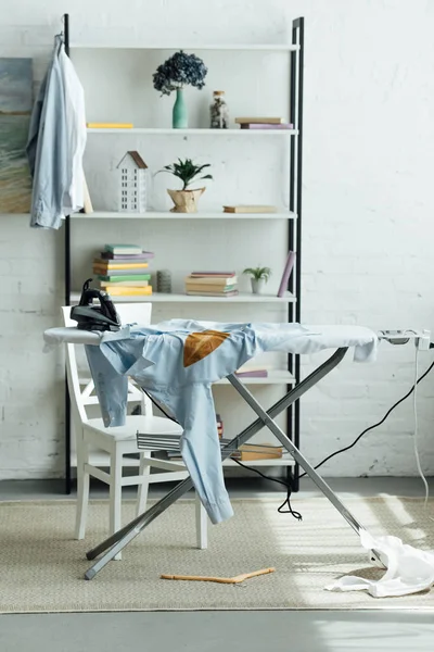 Burned blue shirt and iron on ironing board in living room — Stock Photo