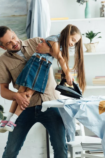 Père portant fille désobéissante et elle veut repasser les vêtements à la maison — Photo de stock