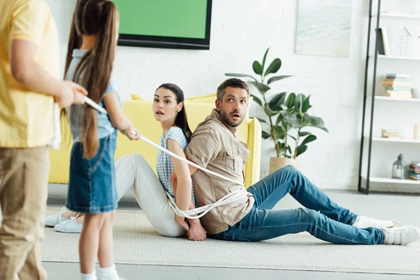 Imagen recortada de los niños atando a los padres con cuerda en el suelo en casa - foto de stock