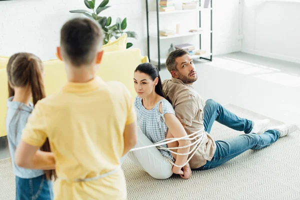 Непослушные дети связывают родителей веревкой на полу дома — стоковое фото