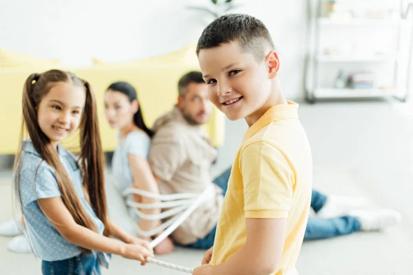 Niños felices atando a los padres con cuerda en el suelo en casa - foto de stock