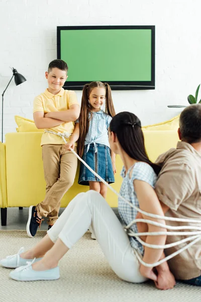 Padres sentados atados con cuerda en el suelo y niños sonrientes mirándolos — Stock Photo