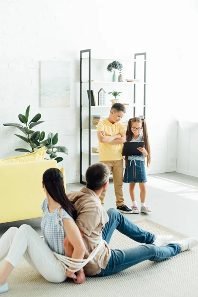 Родители сидят привязанные веревкой на полу и дети держат планшет дома — стоковое фото