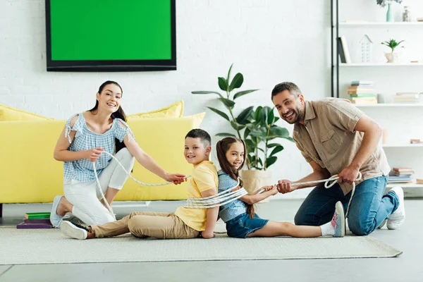 Padres atando a los niños con cuerda en casa y mirando a la cámara - foto de stock