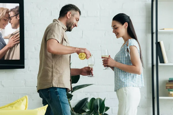 Marito felice versando champagne nei bicchieri in soggiorno — Foto stock