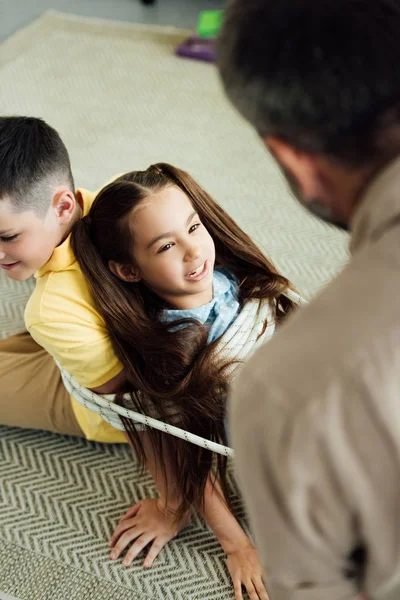 High angle view of father tying children with rope at home, parenthood concept — Stock Photo