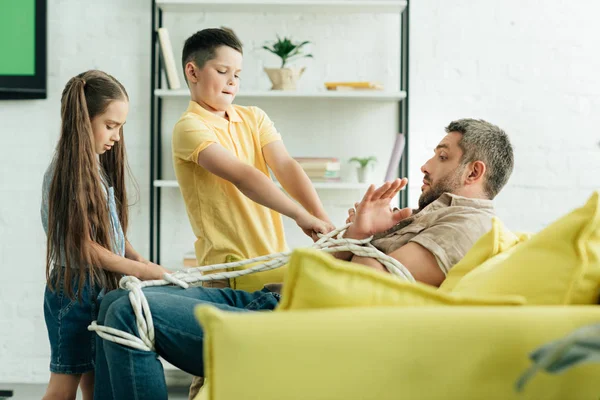 Side view of children tying father with rope at home — Stock Photo