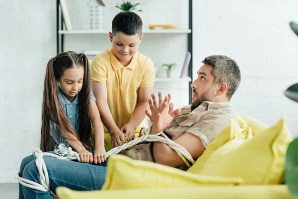 Children tying scared father with rope at home — Stock Photo