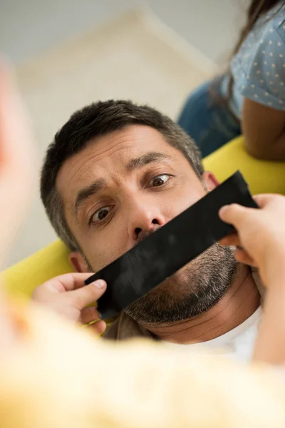 High angle view of children closing father mouth with black tape at home — Stock Photo