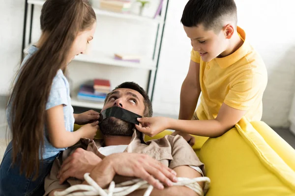 Enfants désobéissants fermer la bouche du père avec du ruban noir à la maison, concept de parentalité — Photo de stock