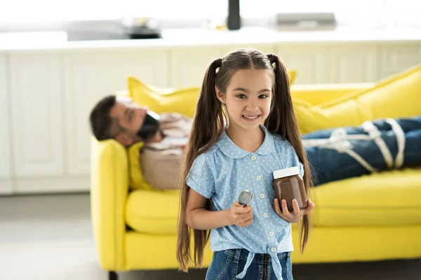 Father lying tied on sofa and smiling daughter holding chocolate at home — Stock Photo