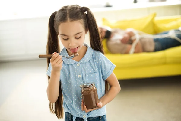 Pai deitado amarrado no sofá e filha comer chocolate em casa — Fotografia de Stock