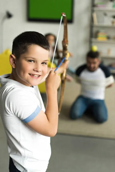 Son playing with tied father and pretending shooting with toy bow at home — Stock Photo