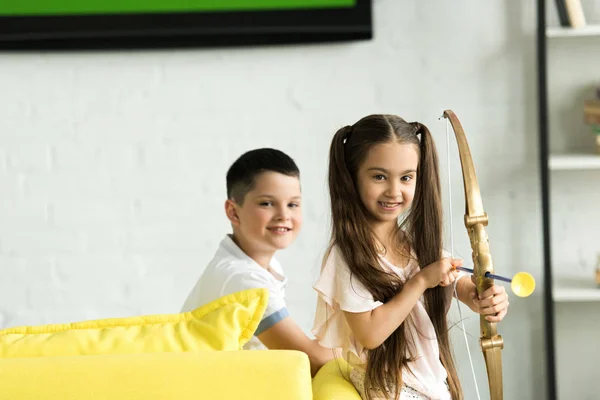 Schwester und Bruder mit Schießspielzeugbogen zu Hause — Stockfoto