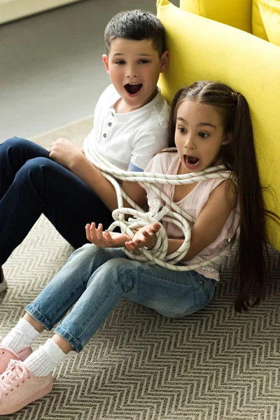 Tied with rope sister and brother sitting on floor and screaming at home — Stock Photo