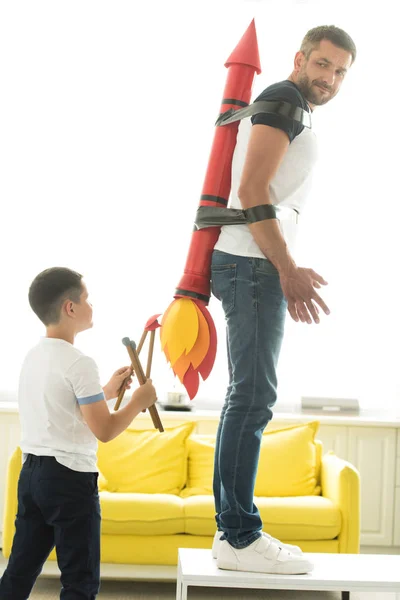 Desobediente hijo jugando con atado padre con cohete juguete en vuelta en casa - foto de stock