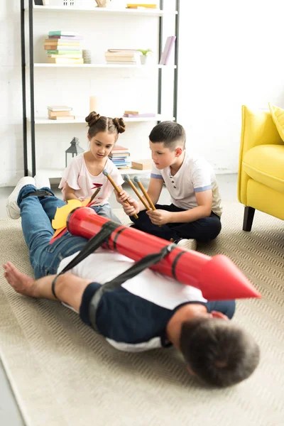 Tied dad with rocket toy lying on floor and children playing with him — Stock Photo