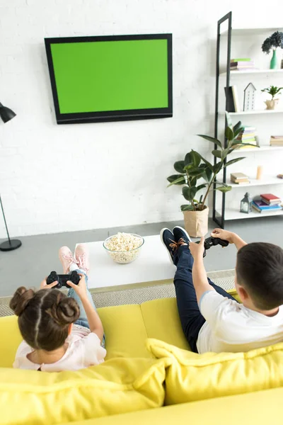 Vista de ángulo alto de la hermana y el hermano jugando videojuego en casa - foto de stock