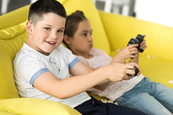 Soeur et frère jouer jeu vidéo sur canapé à la maison — Photo de stock