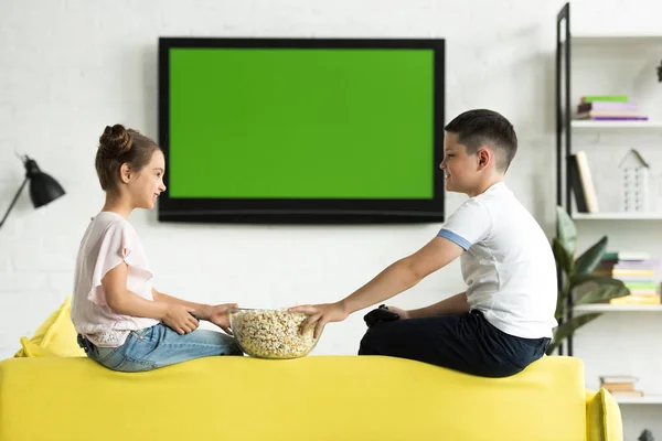 Side view of sister and brother eating popcorn at home — Stock Photo