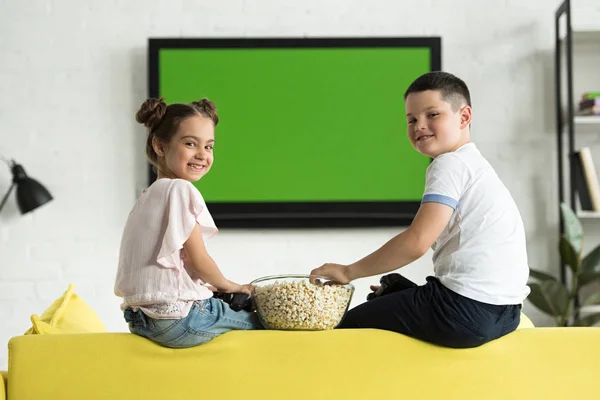 Schwester und Bruder essen zu Hause Popcorn und schauen in die Kamera — Stockfoto