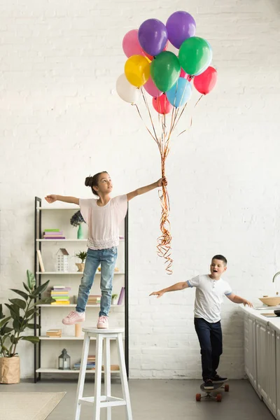 Hermana desobediente y hermano con globos y monopatín en la cocina - foto de stock