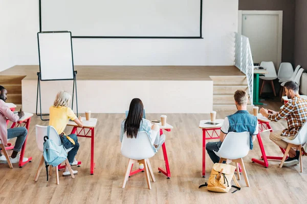 Vista trasera del grupo de jóvenes estudiantes sentados juntos en la sala de conferencias - foto de stock