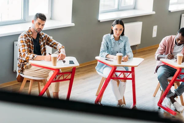 Jóvenes estudiantes concentrados tomando notas y mirando a bordo - foto de stock