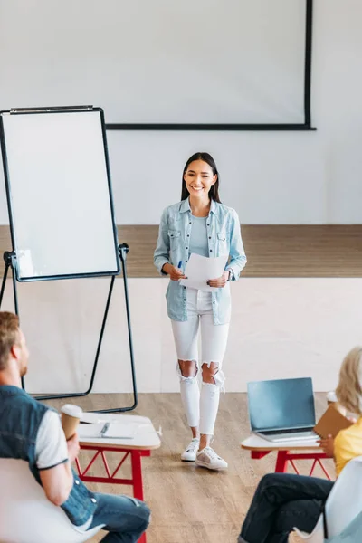 Smiling young asian teacher performing lecture for young students — Stock Photo