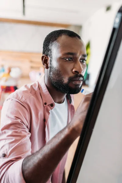 Concentrado joven afroamericano hombre escrito en pizarra blanca - foto de stock