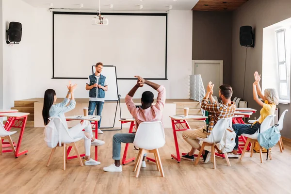 Vista trasera de los jóvenes estudiantes multiétnicos aplaudiendo al profesor después de la presentación en la universidad - foto de stock