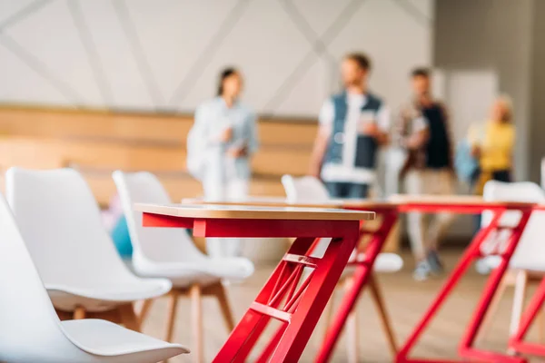 Close-up shot of desks at classroom with blurred group of students on background — Stock Photo