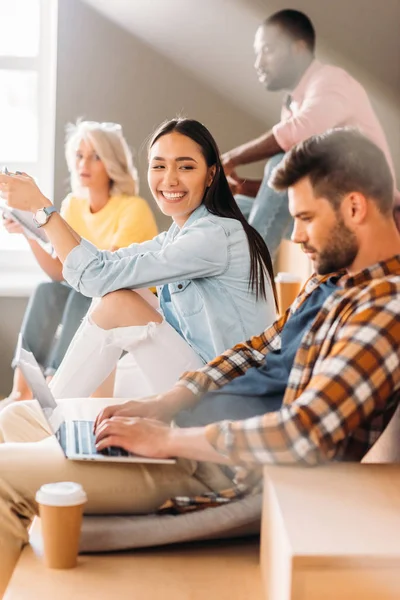 Side view of handsome student using laptop while sitting on tribunes with classmates — Stock Photo