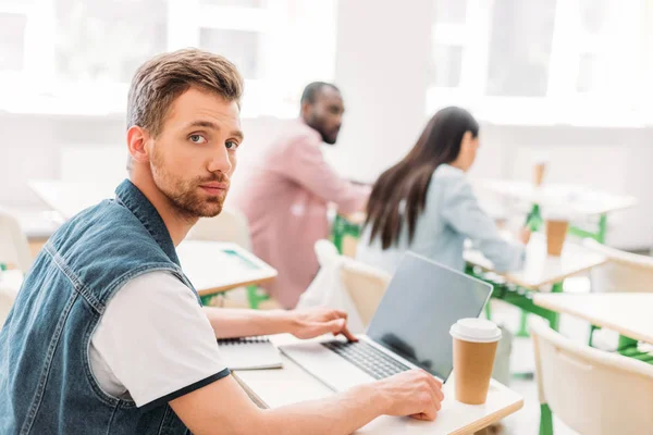 Handsome young student with laptop sitting at classroom — Stock Photo
