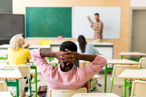 Vue arrière d'un étudiant afro-américain détendu assis en classe pendant les cours — Photo de stock