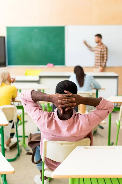Vue arrière d'un étudiant afro-américain détendu assis en classe pendant les cours — Photo de stock
