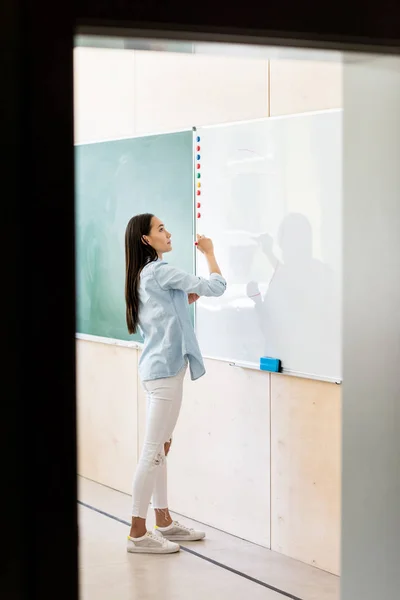 Thoughtful asian student girl writing on whiteboard during lesson — Stock Photo