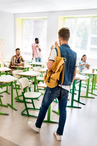 Vue arrière du jeune étudiant dans la salle de classe du collège avec des camarades de classe flous sur fond — Photo de stock