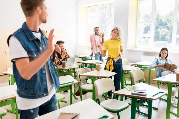 Jóvenes estudiantes saludándose en el aula - foto de stock