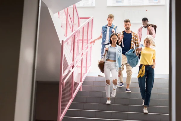 Jóvenes estudiantes con estilo que bajan por las escaleras del pasillo de la universidad - foto de stock