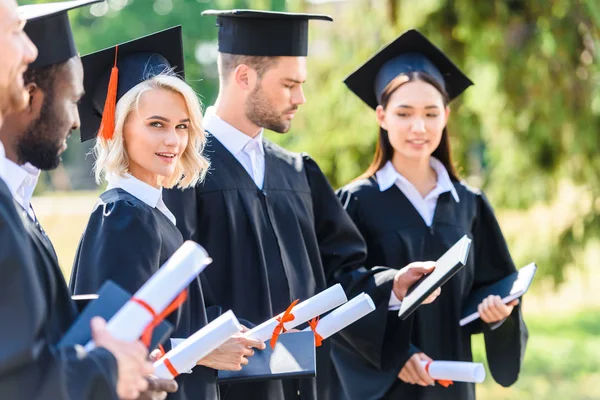 Successful graduated students in capes and hats holding rolled diplomas — Stock Photo